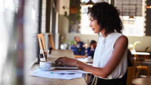 A woman sits at a counter in a cafe, working on a laptop with documents about inheritance law and a cup of coffee in front of her.