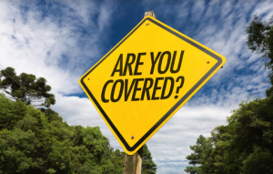 A yellow diamond-shaped road sign with the words "ARE YOU COVERED?" in bold black letters, set against a backdrop of trees and a partly cloudy sky—a reminder to check your third-party auto insurance for damages and insurance claims.