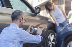 A man takes a photo of damage on a car while a woman points at the damaged area after a minor car accident, documenting everything as recommended by Fears Law.