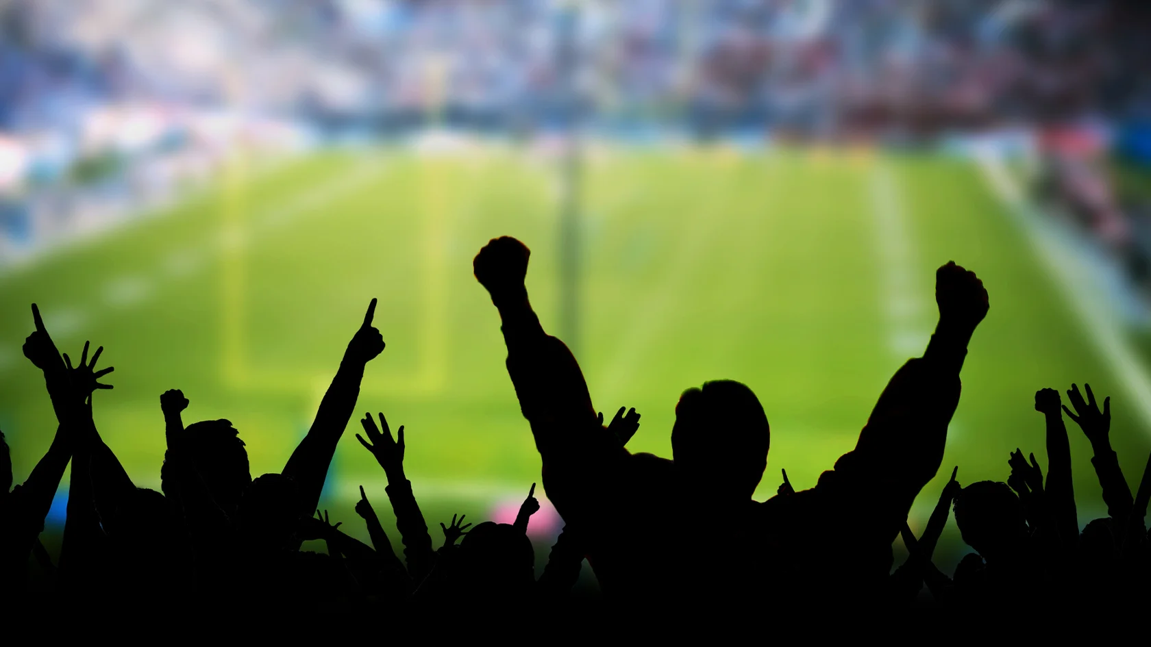 Silhouetted crowd cheering in stadium stands with a blurred football field visible in the background, highlighting the excitement of game day and emphasizing the importance of Stadium Safety for all fans.