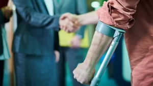 A person using crutches stands in the foreground, while two people in business attire shake hands in the background—highlighting the importance of not waiting too late to file a personal injury claim.
